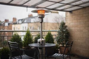 Frau sitzt gemütlich auf ihrem überdachten Balkon unter einer flachen Heizstrahler-Lampe und genießt warme Abende im Freien.