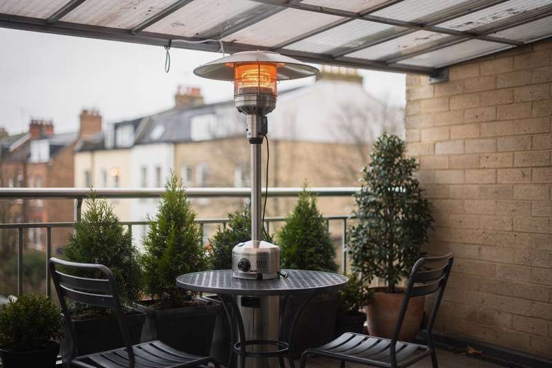 Frau sitzt gemütlich auf ihrem überdachten Balkon unter einer flachen Heizstrahler-Lampe und genießt warme Abende im Freien.