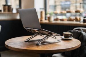 Frau mit Laptop auf Ständer sitzt an Café-Tisch mit Kaffee und arbeitet konzentriert.