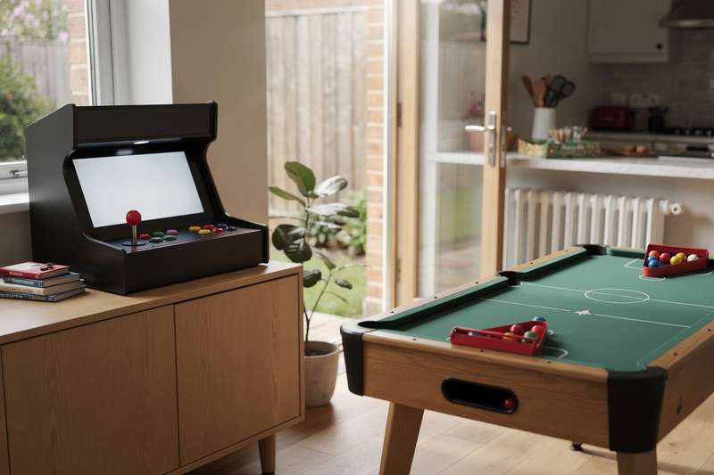 Freunde spielen gemeinsam an einem Arcade-Automaten im Wohnzimmer.