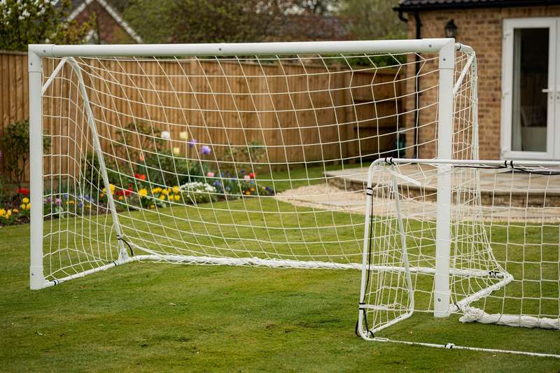 Kinder spielen Fußball vor einem Trainingstor im heimischen Garten.