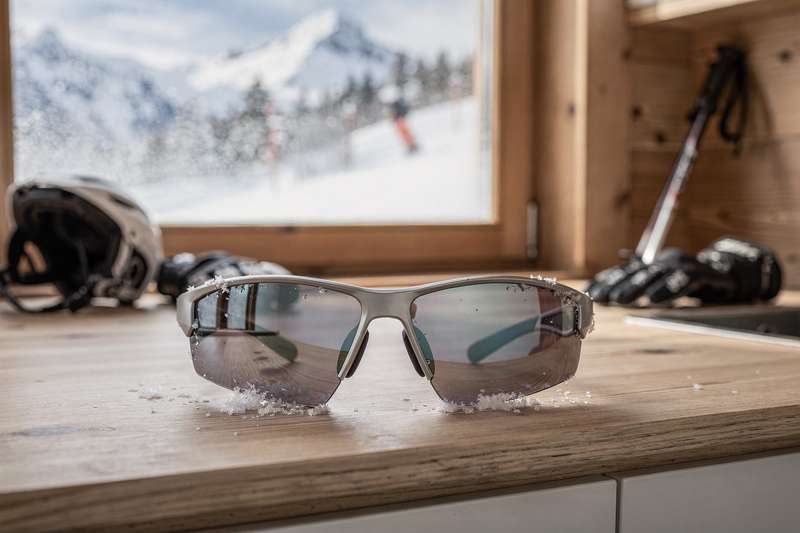 Skifahrer mit Sonnenbrille fährt bei Sonnenschein die schneebedeckte Piste hinab.