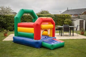 Eine Hüpfburg mit bunten Spielbereichen steht in einem grünen Garten, während Kinder darin springen und lachen.